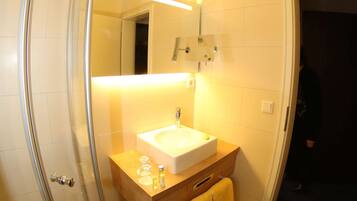 A bathroom with a glass shower enclosure, a sink, and a mirror.