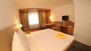 Habitación de hotel con cama, escritorio, silla, televisor y ventana con cortinas.