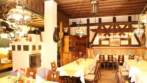 Un restaurante con mesas y sillas de madera, techo alto con vigas a la vista y diversas lámparas colgantes.