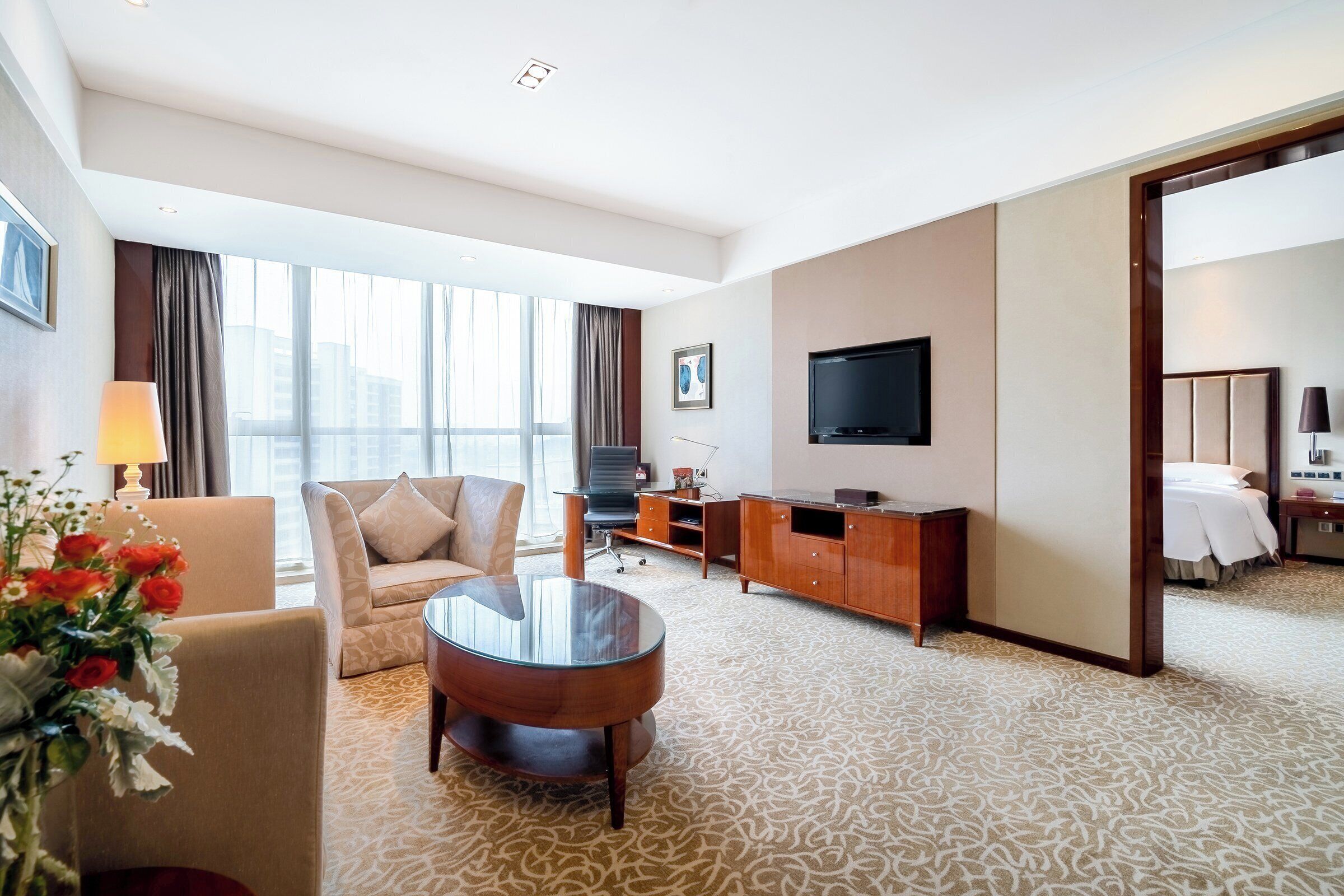 Ein Hotelzimmer mit einer Couch, einem runden Couchtisch, einem Fernseher, einem Schreibtisch und einem Bett.