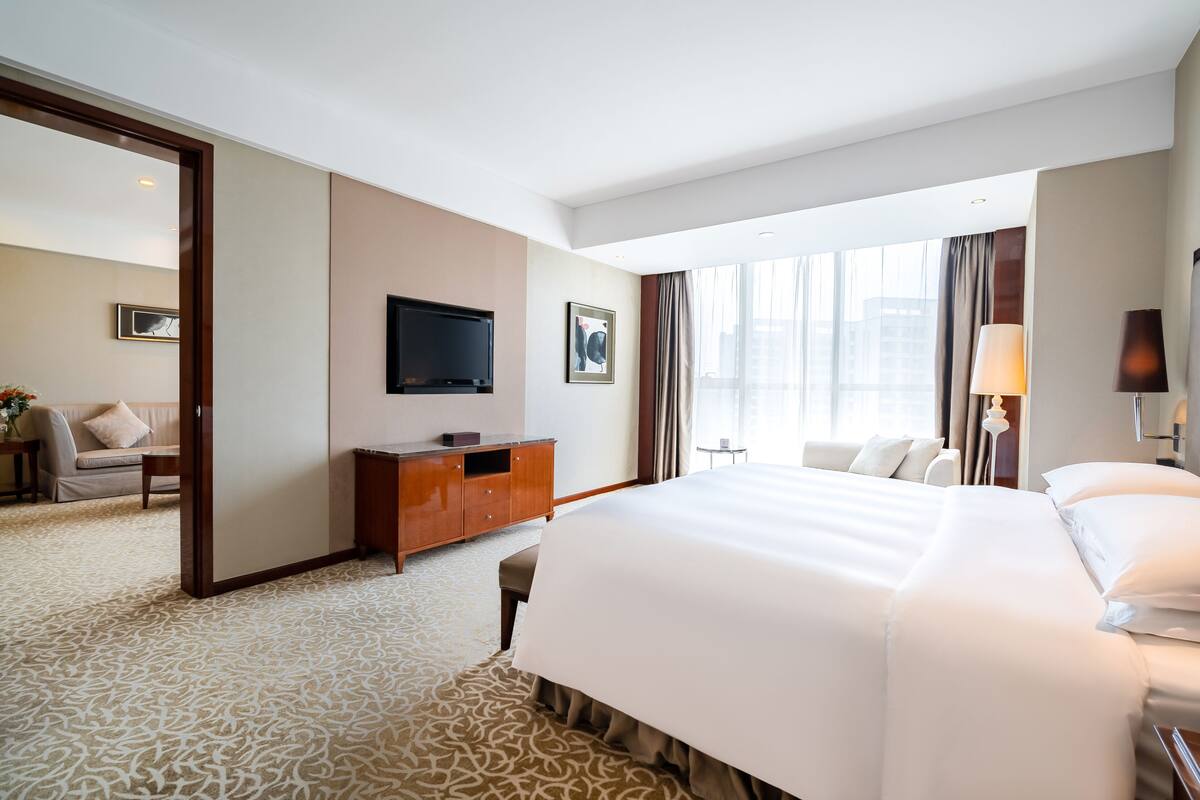 Una habitación de hotel con una cama grande, televisión, escritorio y sofá.