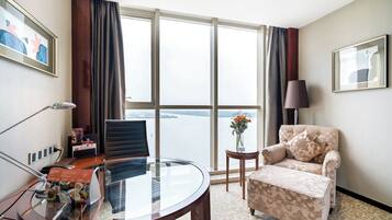 A hotel room with a large window, a round table, a sofa, and a small side table with a vase.