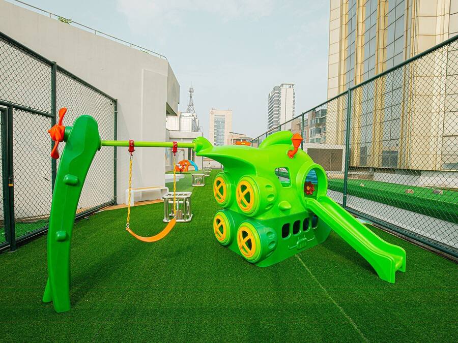 A playground with a slide and climbing structures, surrounded by a chain-link fence and artificial grass.