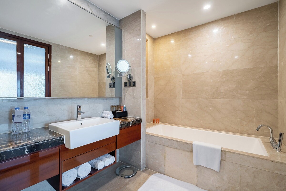 A modern bathroom with a large mirror, a white sink, a bathtub, and a vanity with a marble countertop.