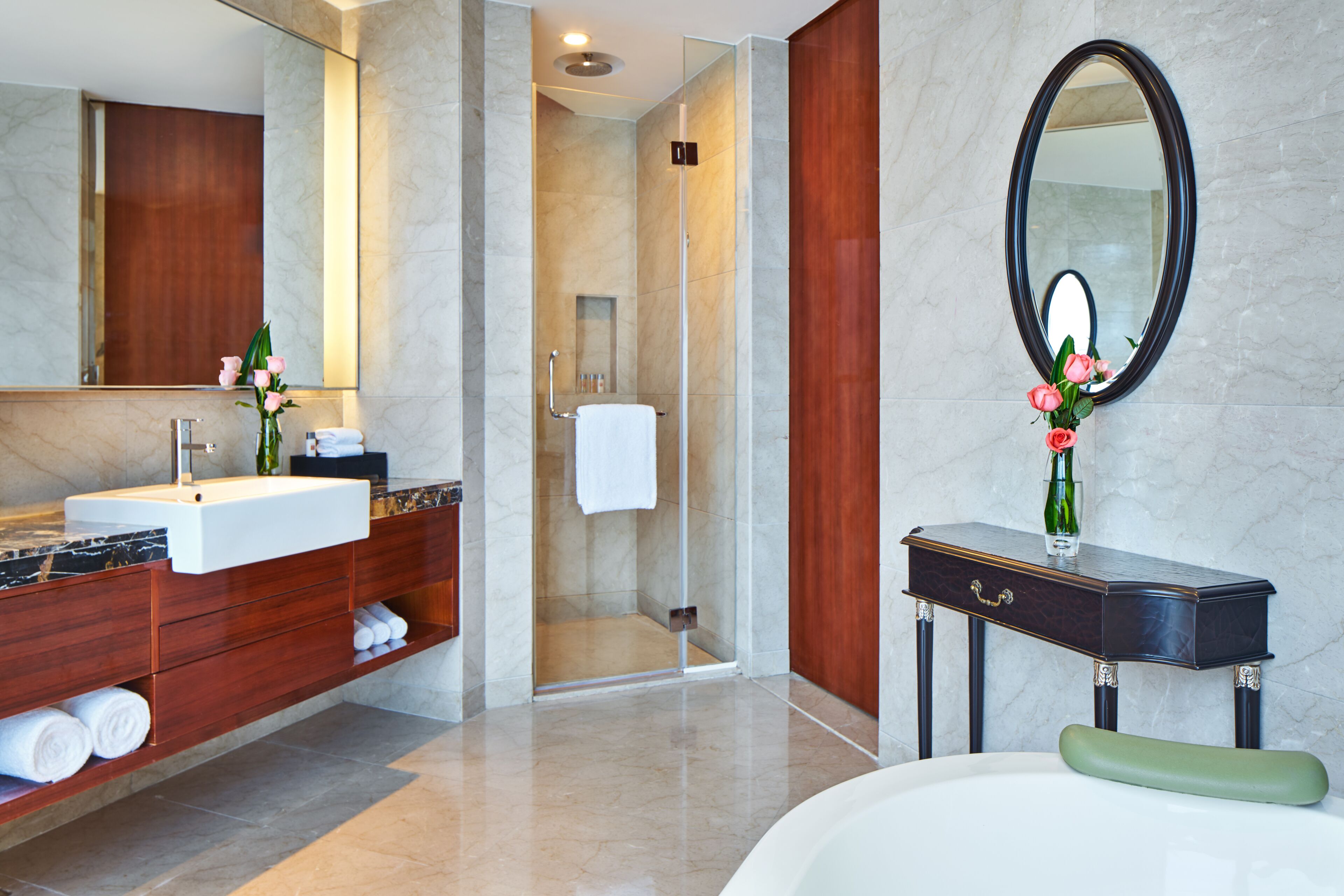 Un baño moderno con lavamanos de mármol, tocador de madera, un espejo grande y una bañera verde.