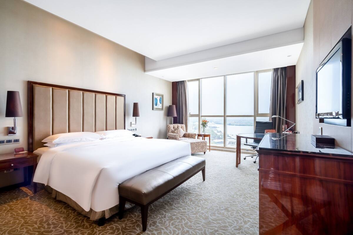 Habitación de hotel con una cama grande, un escritorio, una silla y vistas de la ciudad.