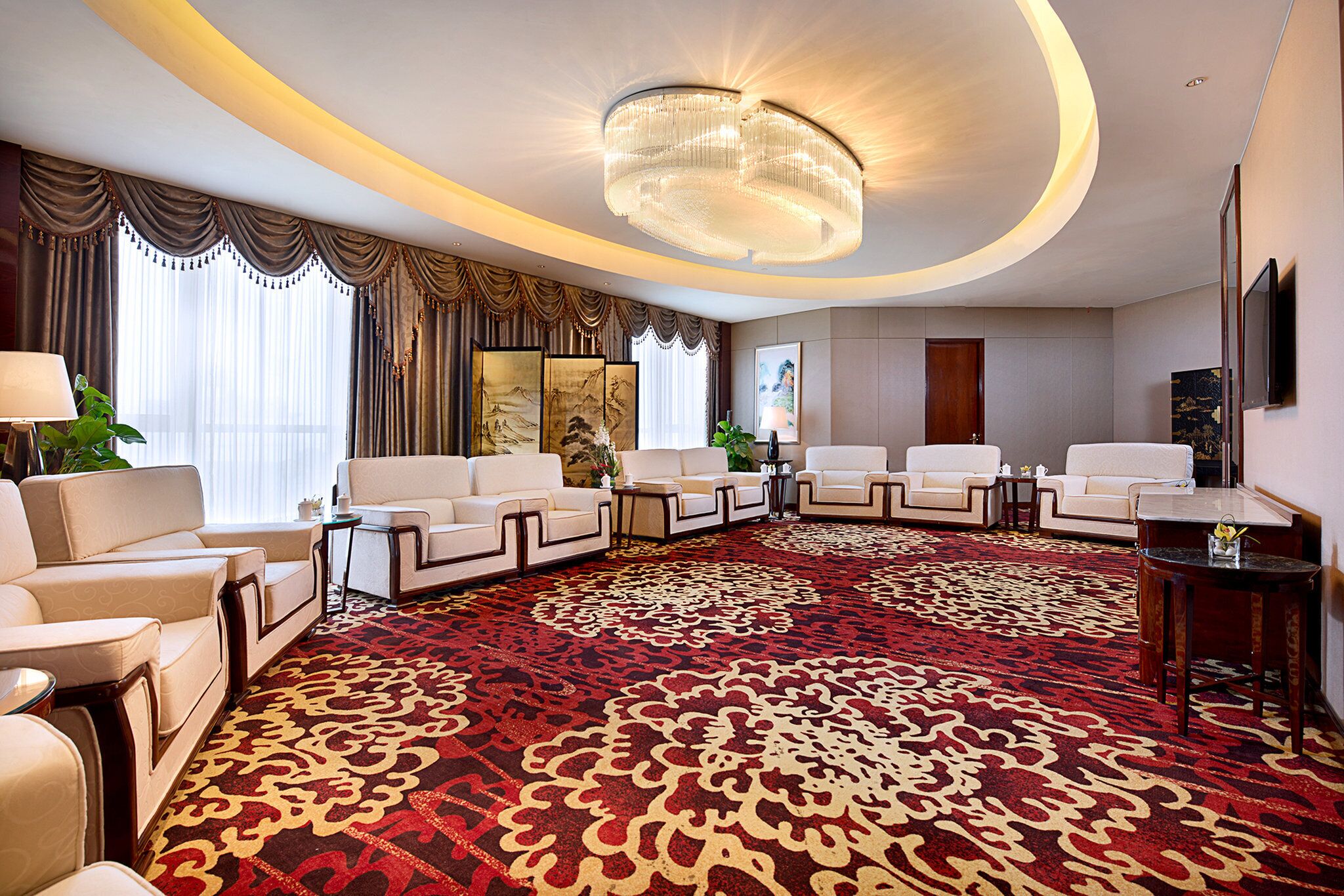 A spacious hotel lobby with a large red carpet, multiple seating areas, and a grand chandelier.