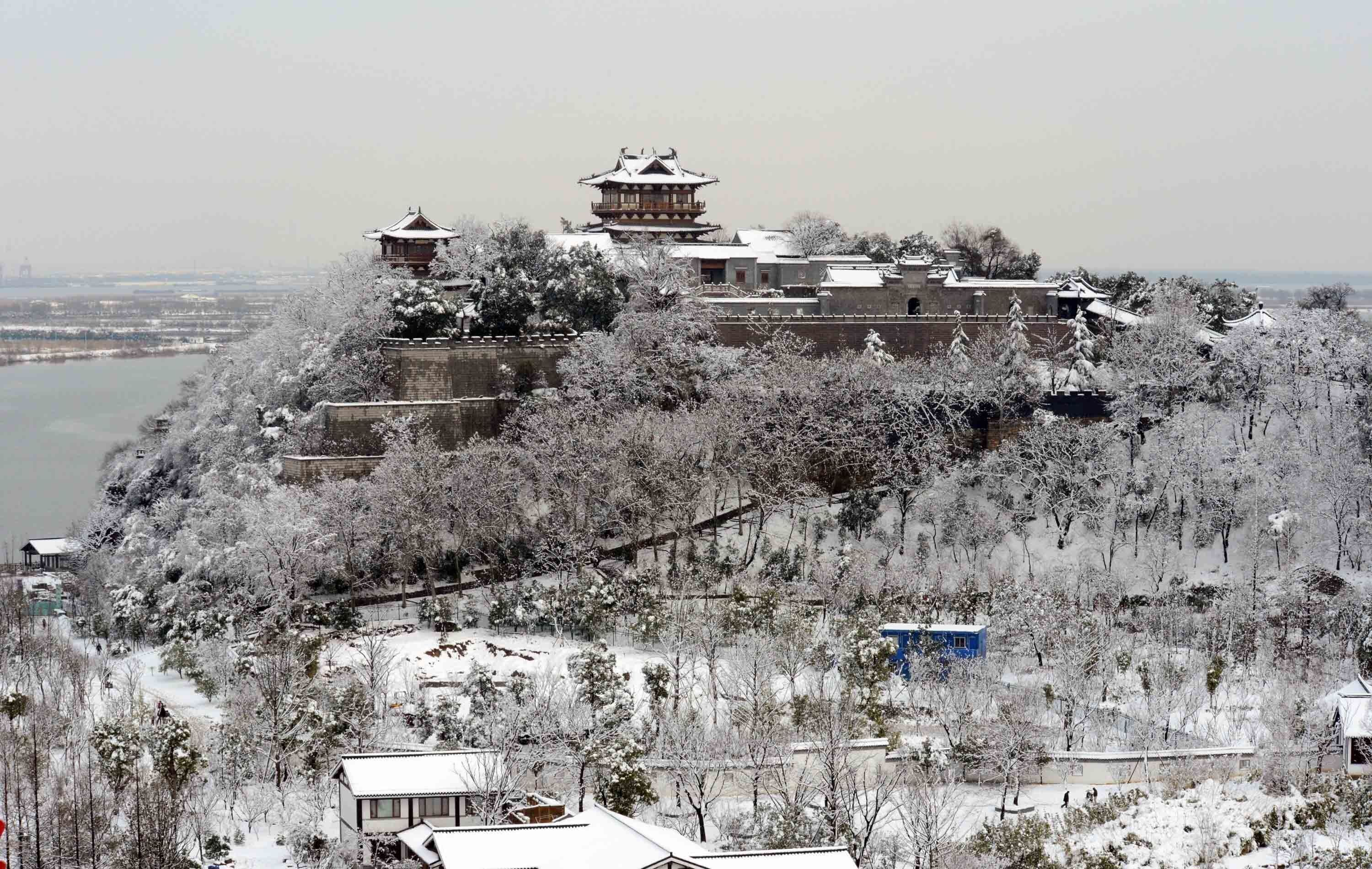 Un edificio tradicional de varios niveles y una imponente torre central, rodeado de árboles nevados y un paisaje ondulado.