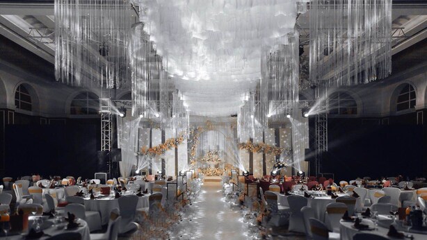 Un salón de banquetes con mesas dispuestas para un evento formal, con un escenario central y elegantes arreglos florales.