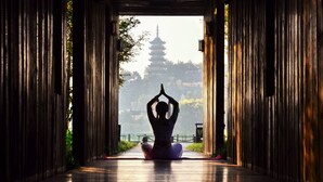 Una persona en posición meditativa en un corredor con arquitectura tradicional y una pagoda al fondo.