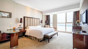 A hotel room with a large bed, a desk with a lamp, a television, and a view of the city.