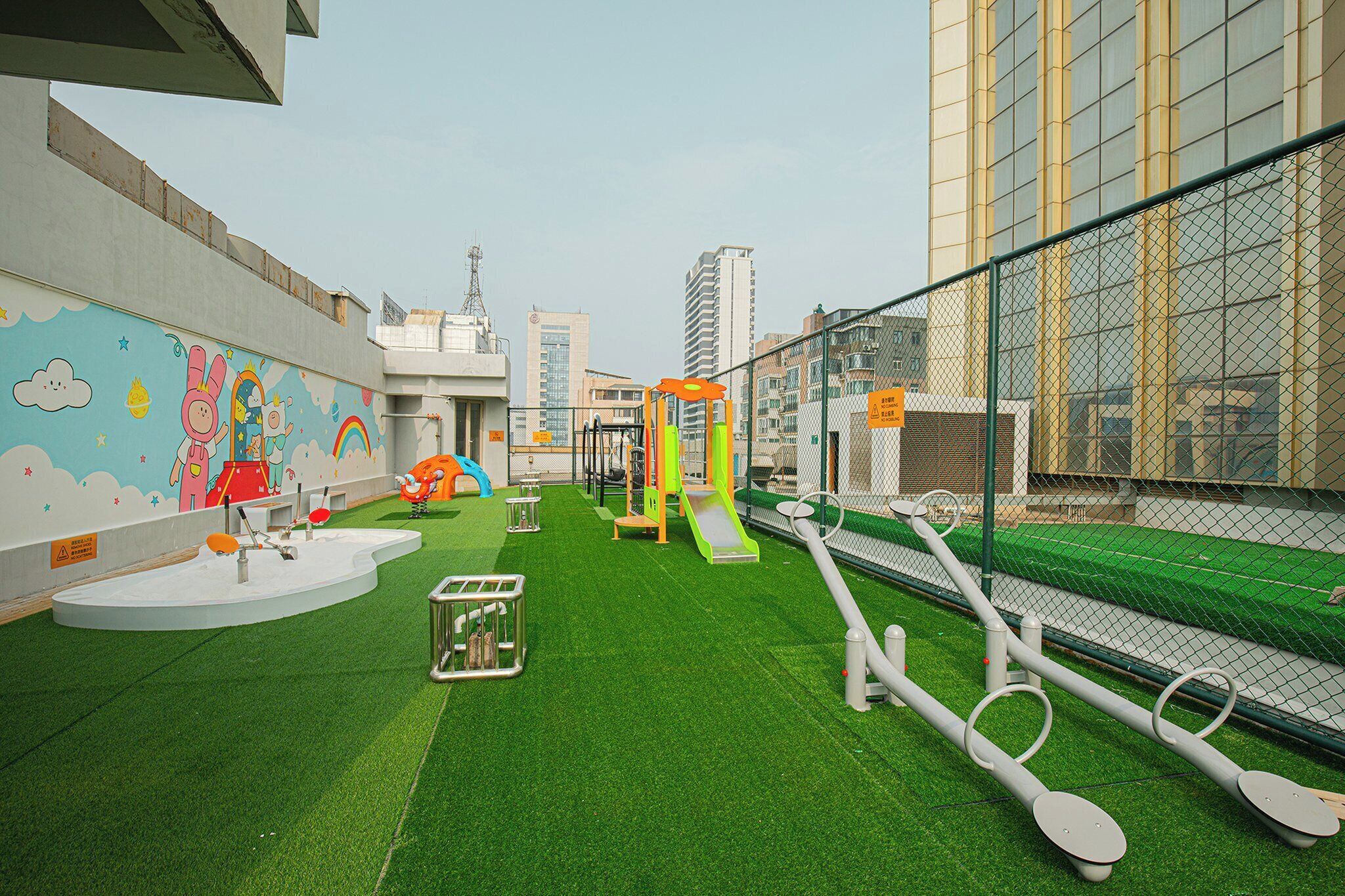 An indoor playground with artificial grass, play structures, and a mural on the wall.