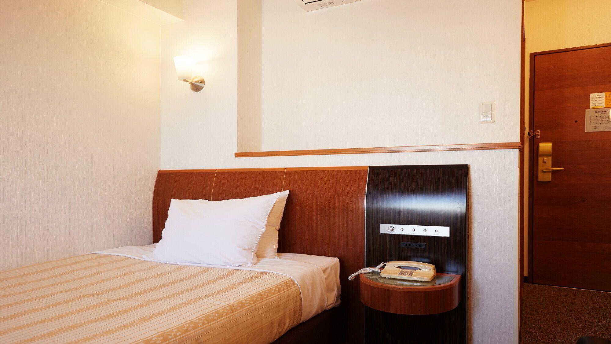 A hotel room with a bed, a bedside telephone, and a wall-mounted light fixture.