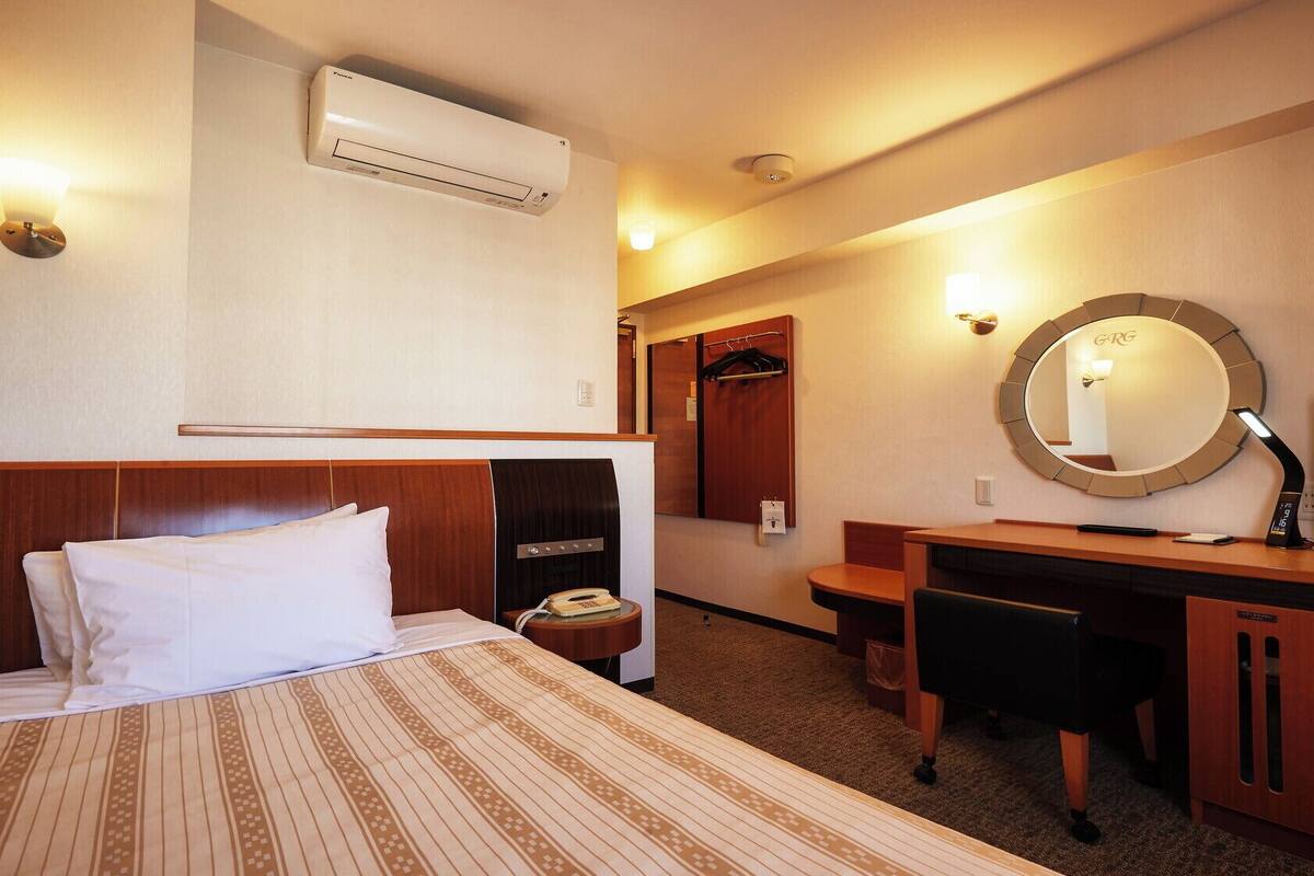 A hotel room with a bed, desk, TV, and a mirror.