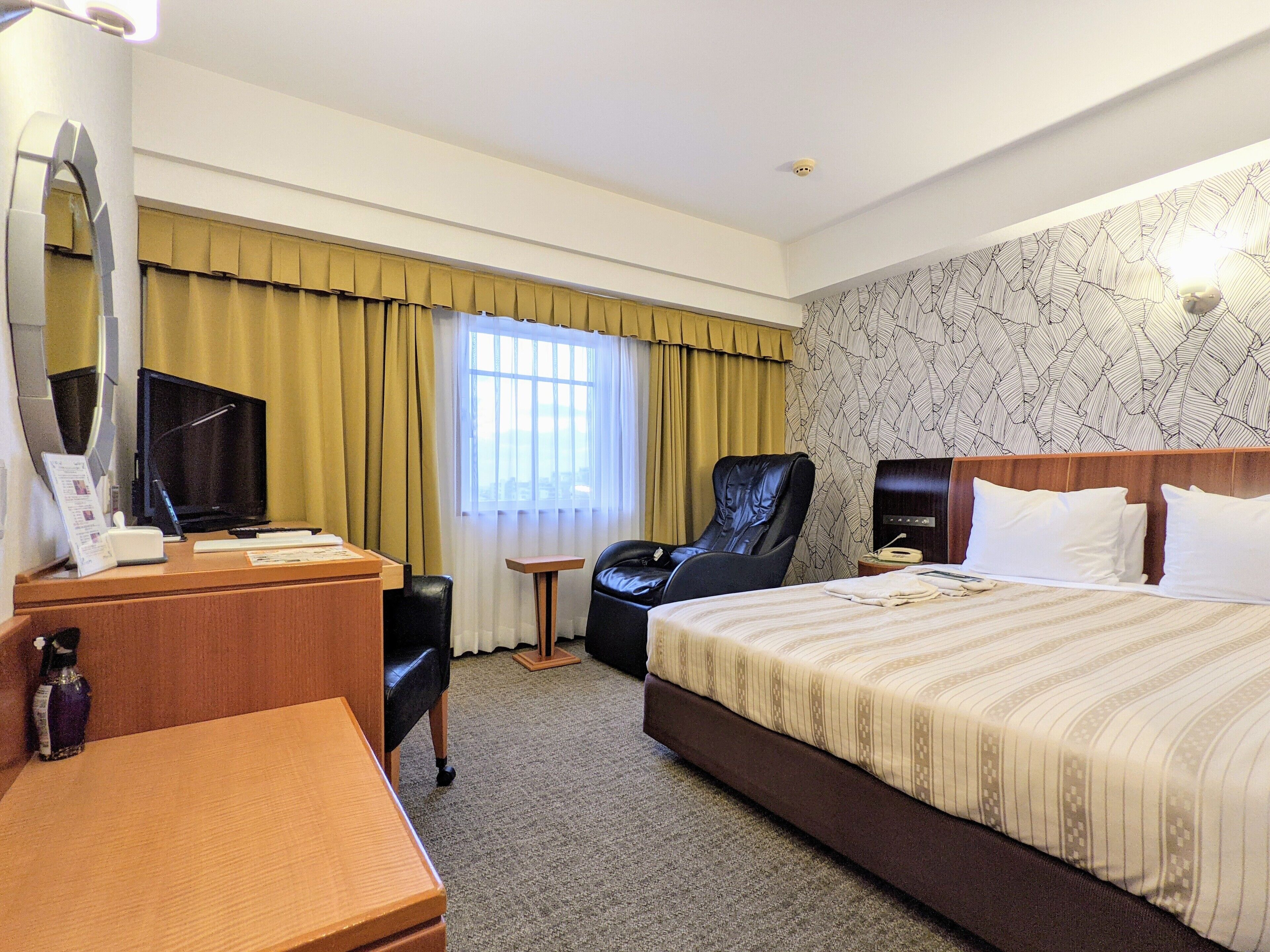 A hotel room with a bed, a desk, a chair, a television, and a window with curtains.