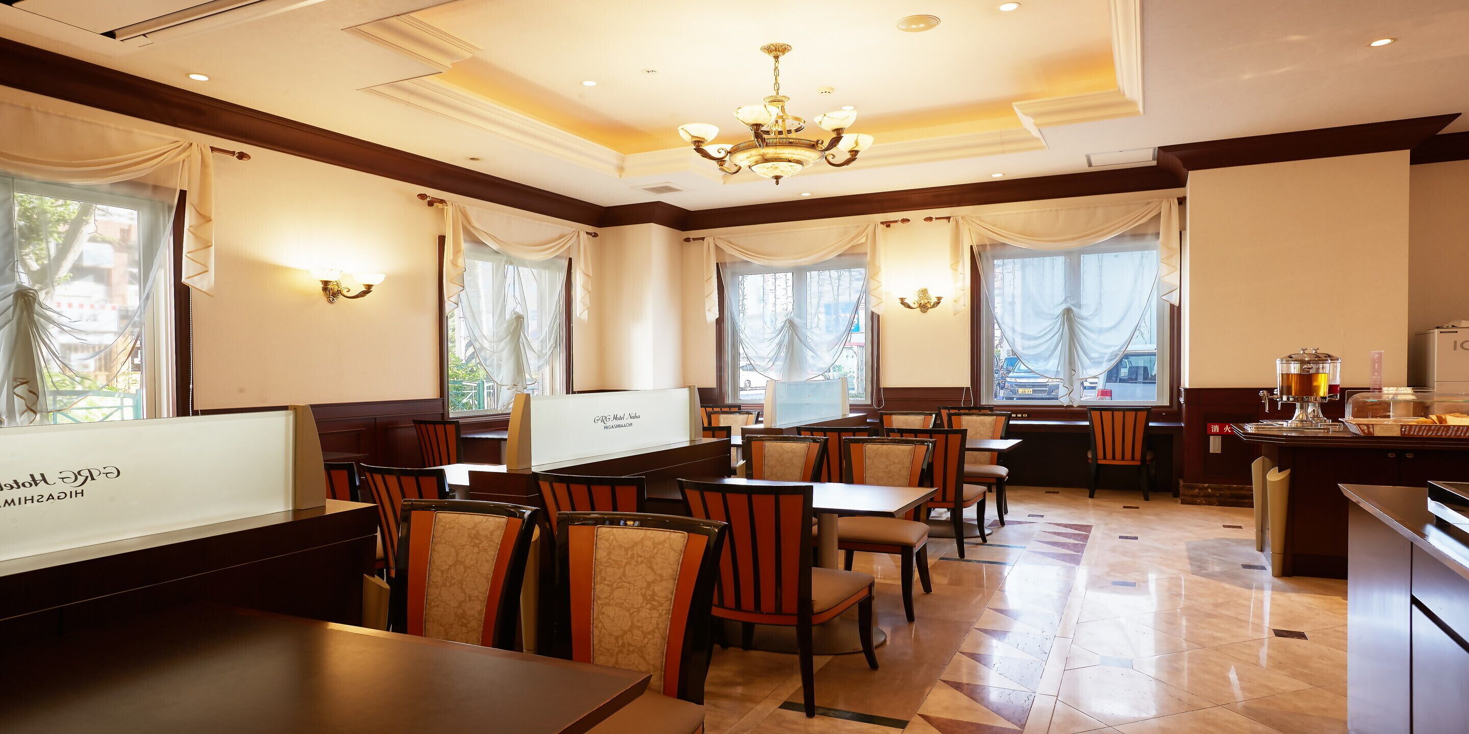 En hotelrestaurant med flere borde og stole, en lysekrone og store vinduer med gardiner.