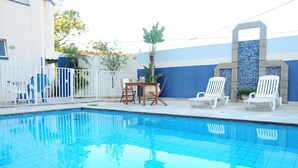Une piscine avec un revêtement de sol en carrelage, une clôture blanche et une table avec des chaises.