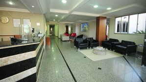 Un hall d’hôtel comprenant un comptoir d’accueil, un espace salon et une horloge murale.