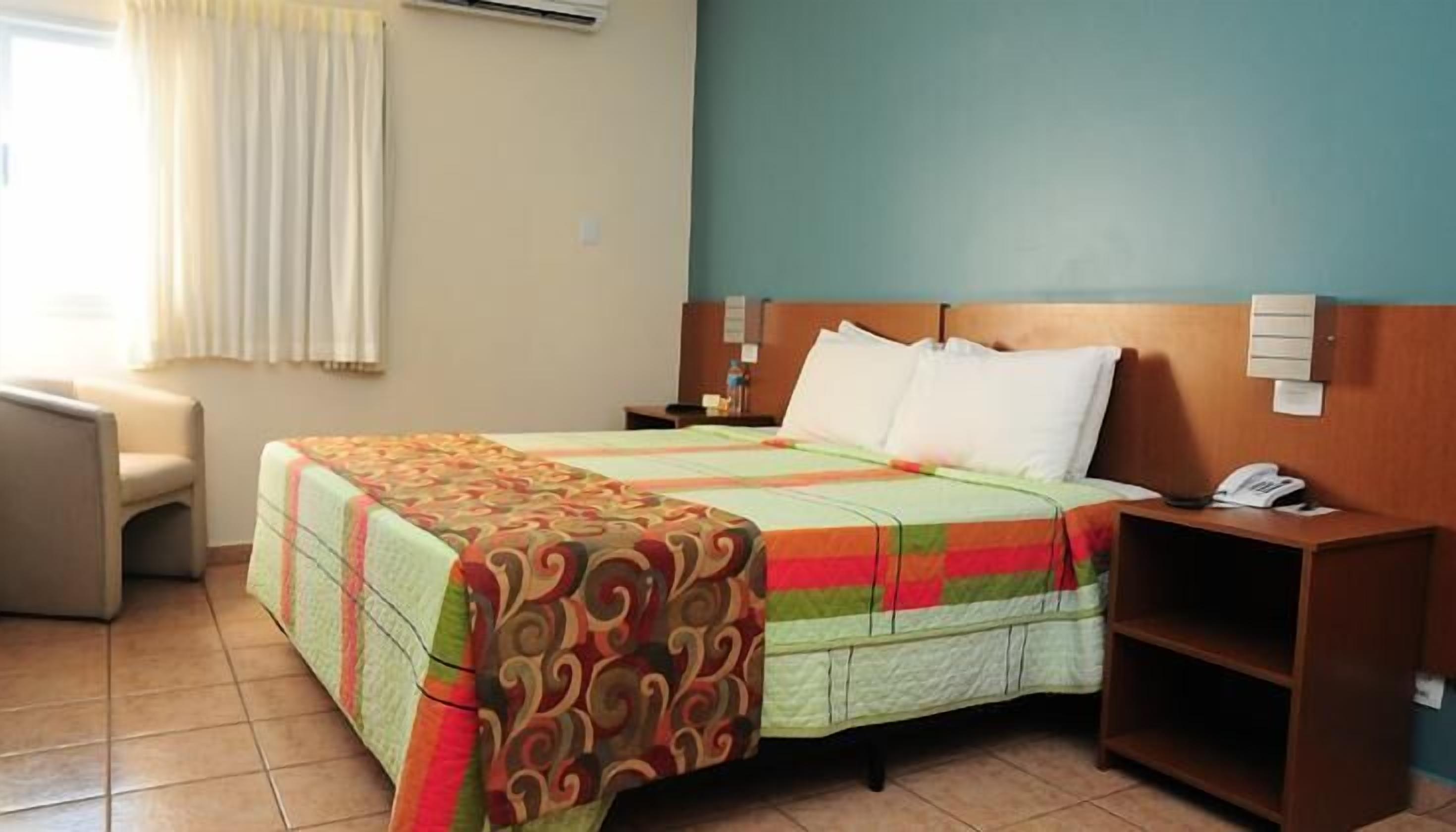 A hotel room with a bed, a nightstand, a chair, and a desk.