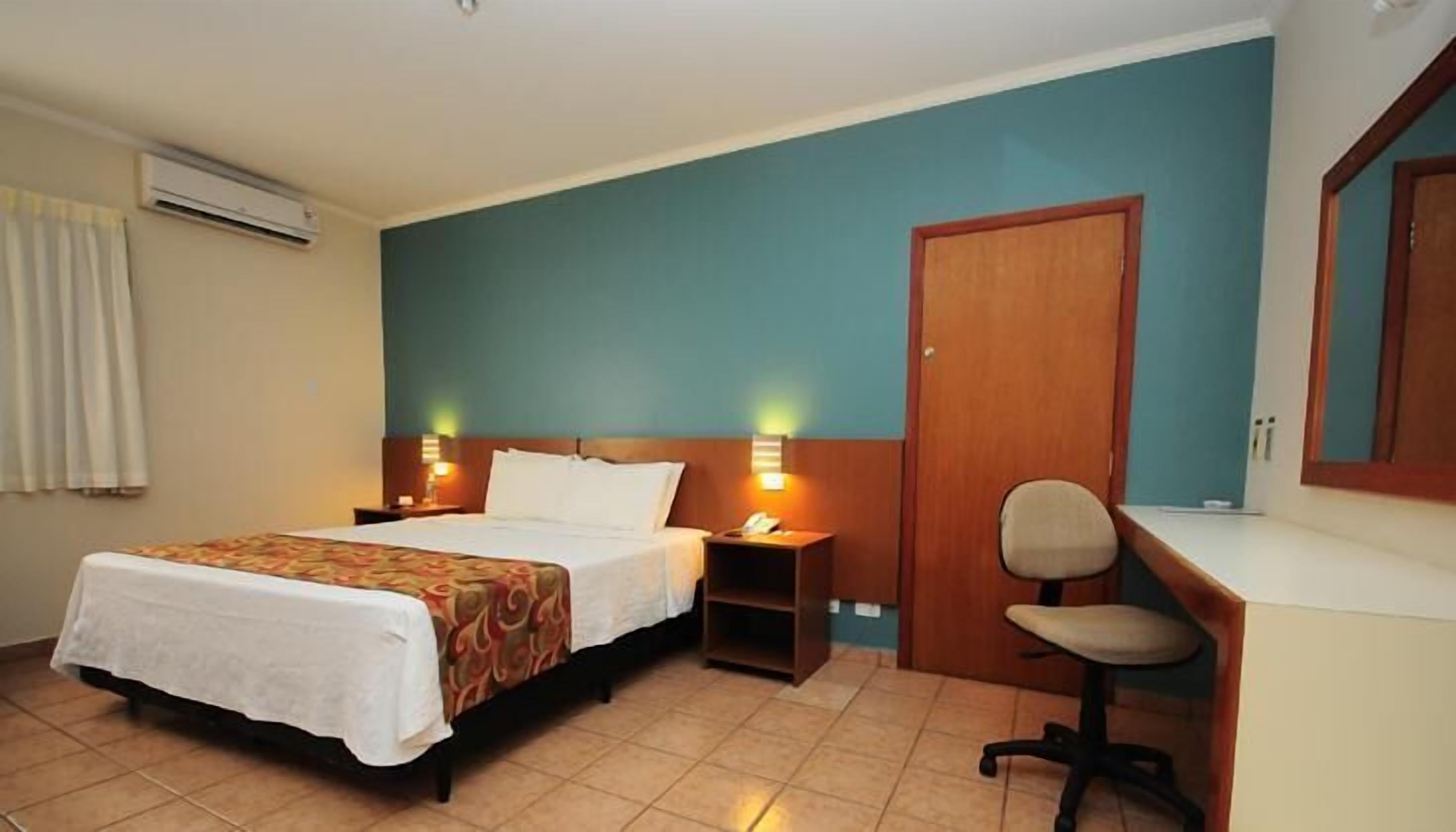 Una habitación de hotel con una cama, mesitas de noche, un escritorio y una silla.
