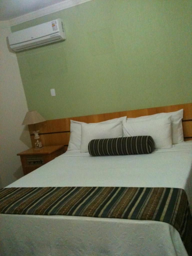 Een hotelkamer met een bed, een nachtkastje, een lamp en een airconditioning aan de muur.
