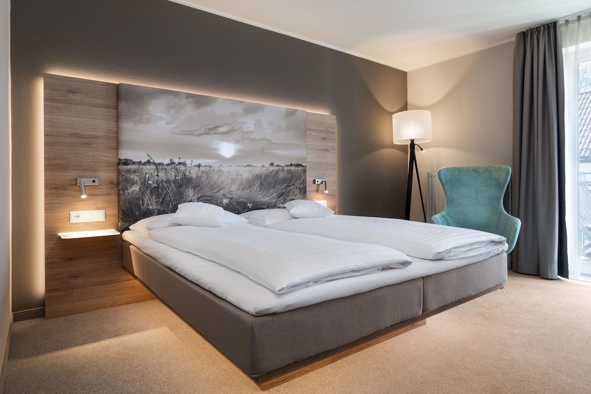 Une chambre d’hôtel moderne avec un grand lit, une table de chevet, une lampe et une vue sur l’extérieur.