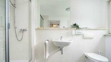A bathroom with a glass shower enclosure, a white sink, and a toilet.