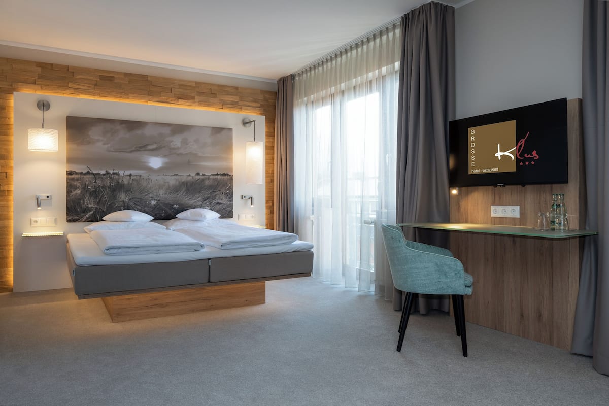 Une chambre d’hôtel moderne équipée d’un lit, d’un bureau, d’une télévision et d’une grande fenêtre avec des rideaux.