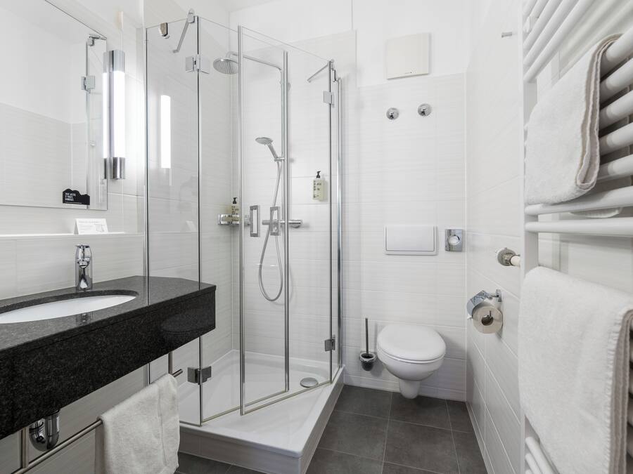 Un baño moderno con ducha de vidrio, un lavamanos blanco y un inodoro.