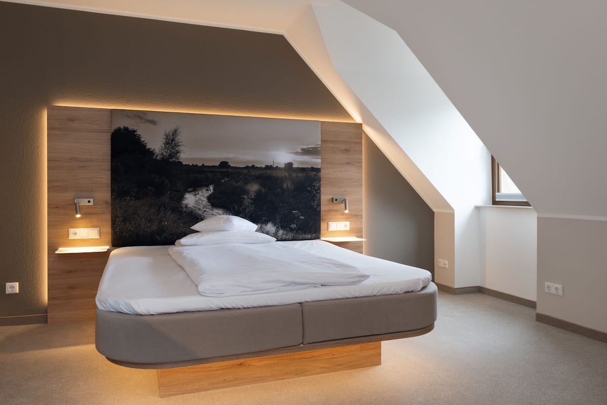 Une chambre moderne avec un lit intégré, un grand tableau représentant un paysage accroché au mur et un plafond en pente.