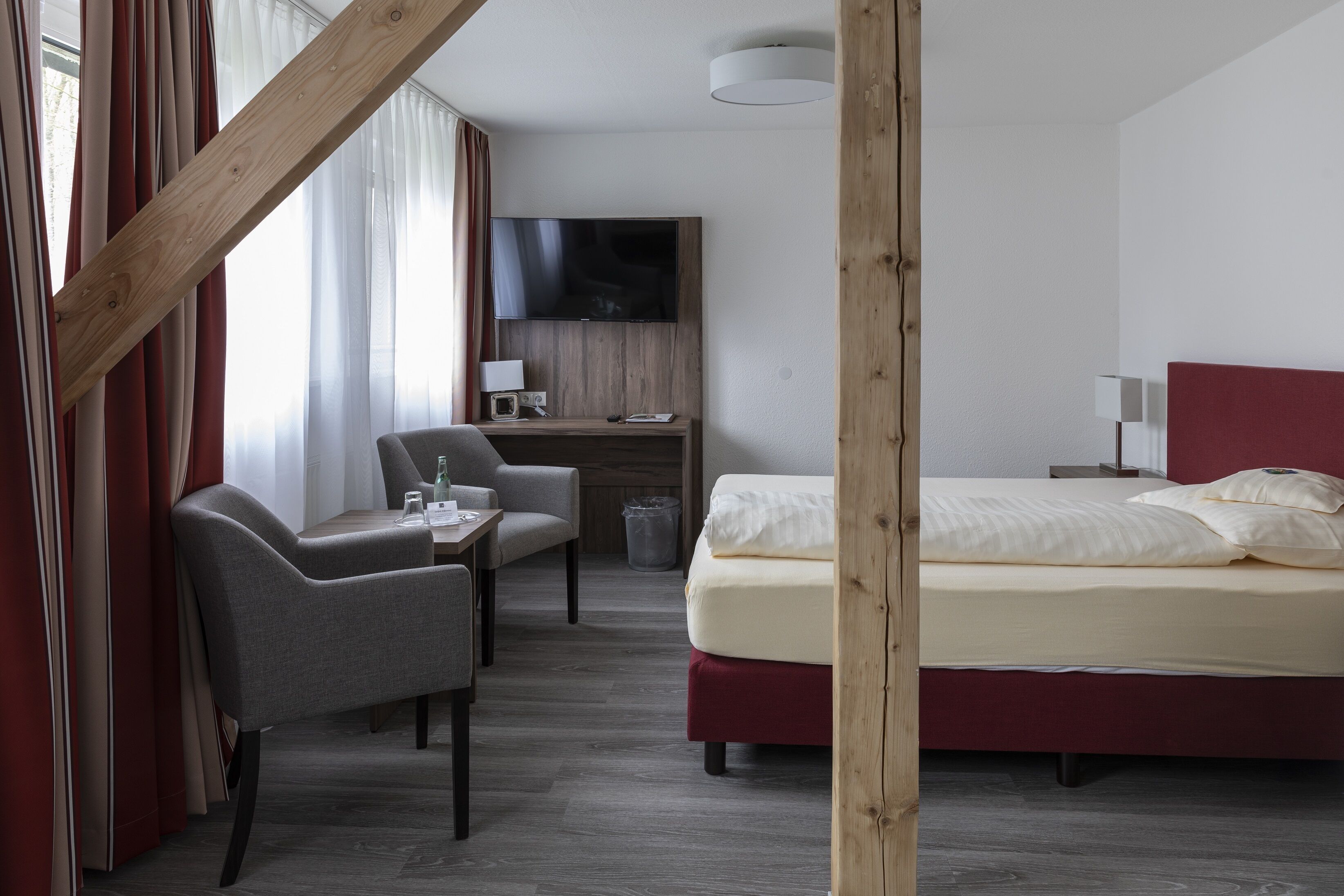 A hotel room with a bed, a desk with a computer, a chair, and a TV mounted on the wall.