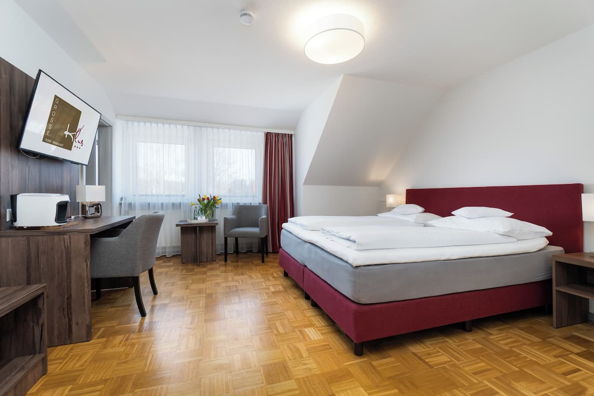 Une chambre d’hôtel avec un lit, un bureau, une chaise et une petite table sur laquelle est posé un vase de fleurs.
