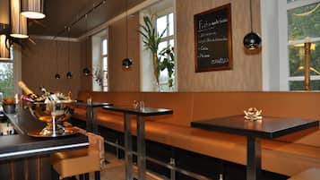 Ein Restaurantinnenraum mit Holzwänden, schwarzen Tischen und orangefarbenen Sitzbänken.
