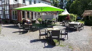 Eine Terrasse im Freien mit Tischen und Stühlen, einem großen grünen Sonnenschirm und einem weißen Zelt.