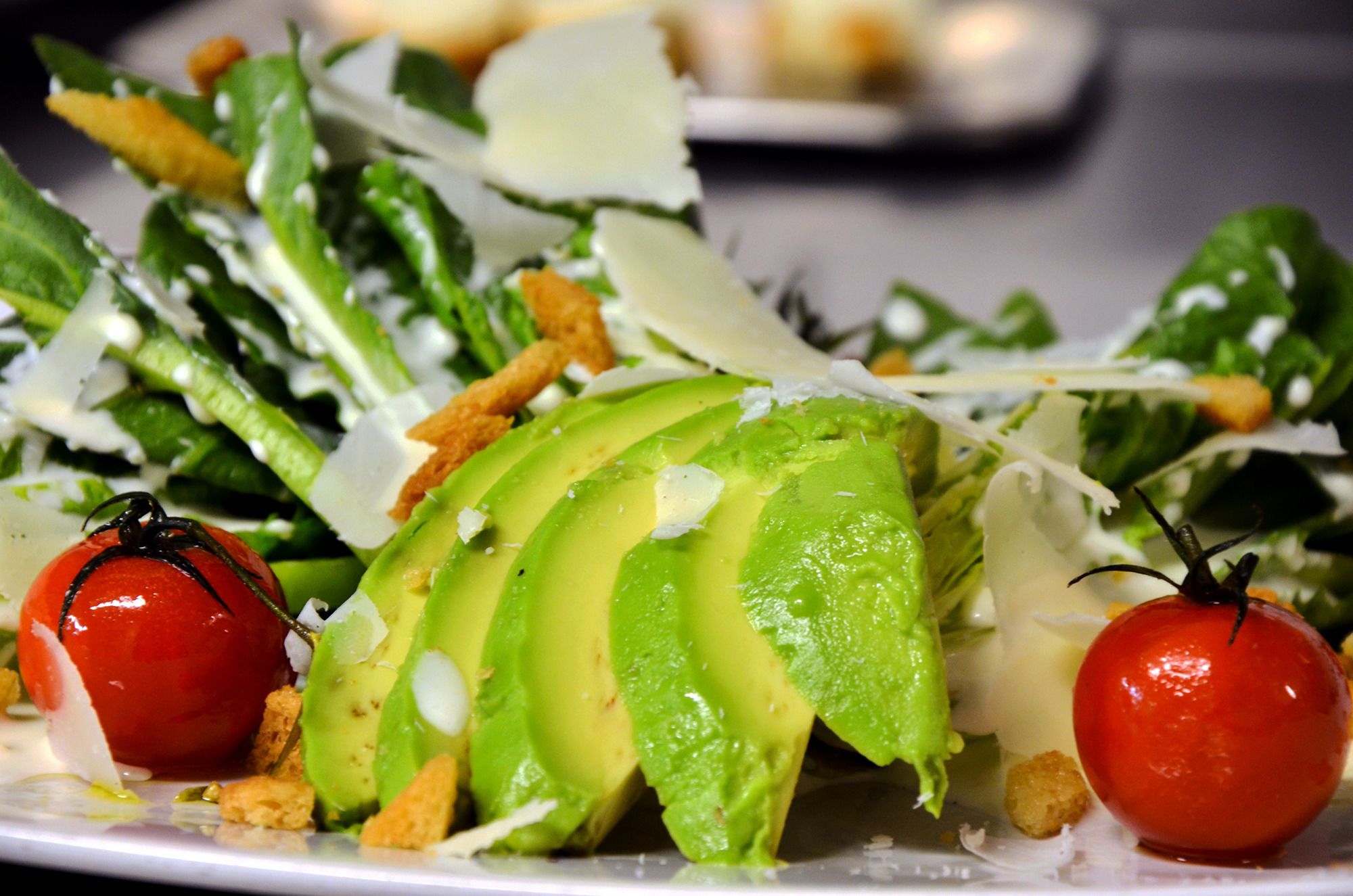 A salad with avocado slices, cherry tomatoes, and croutons on a plate.