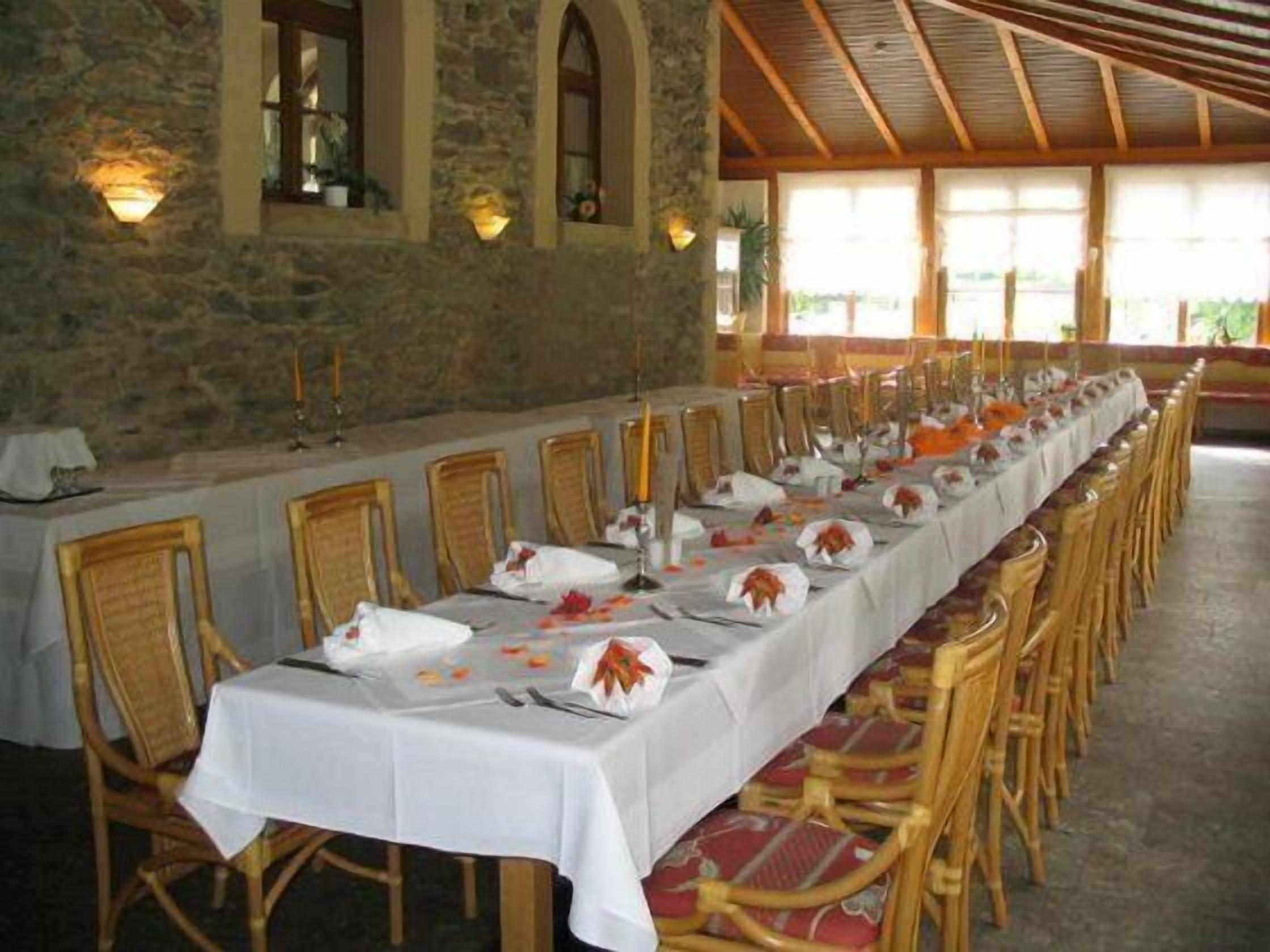 Uma longa mesa de jantar posta com toalhas brancas, cadeiras de madeira e velas.