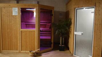 A sauna room with wooden walls and a glass door, a bench, and a potted plant.