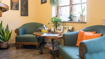 Uma sala de estar acolhedora com dois poltronas verdes, uma mesa de centro de madeira e uma janela com plantas em vasos.