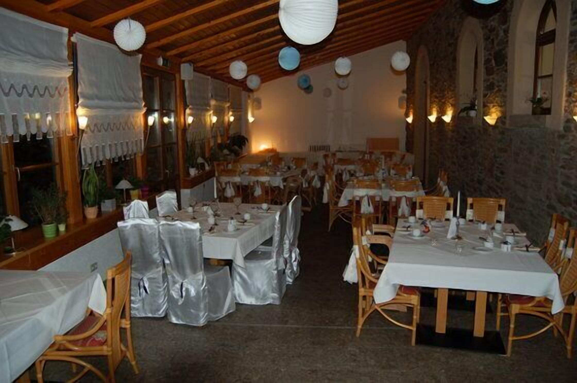 Un restaurante con varias mesas y sillas, vigas de madera en el techo y paredes de piedra.