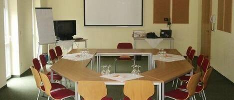 A conference room with a large table, red and yellow chairs, a projector screen, and a whiteboard.
