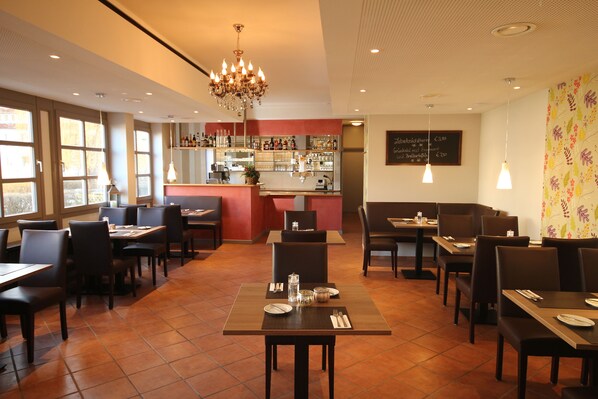 A restaurant with multiple tables and chairs, a bar area, and a chandelier. - Hotel Rennschuh (Goettingen)