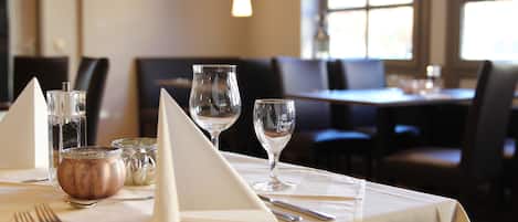 Una mesa de restaurante con mantel blanco, vasos transparentes, una jarra de cobre y una servilleta doblada.