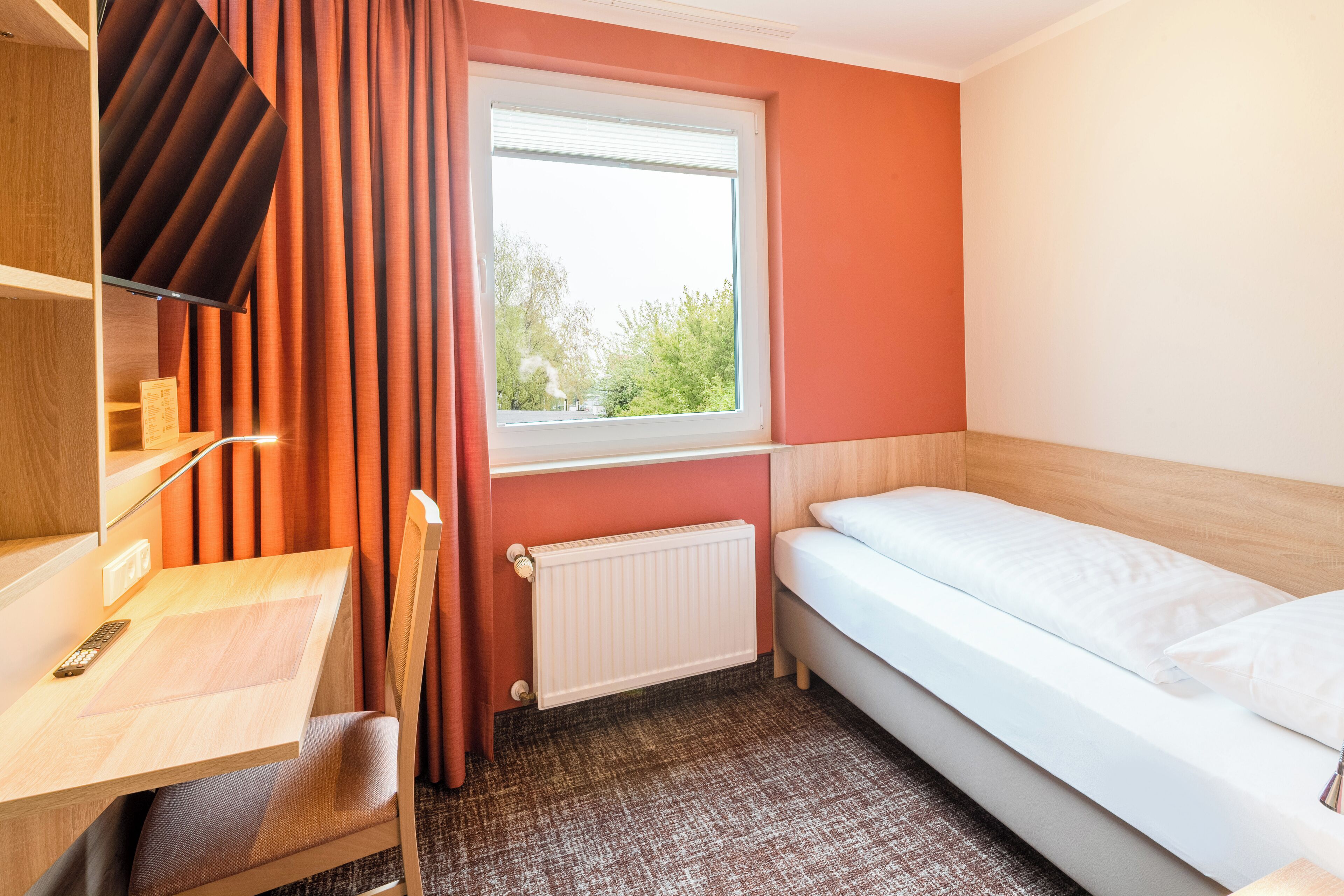Hotelkamer met een bed, een bureau, een stoel, een raam met gordijnen en een radiator.
