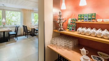 Un coin repas avec une table dressée pour deux personnes, un espace dédié à la préparation du thé avec des théières et des tasses, et une vue sur l’extérieur grâce à de grandes fenêtres.