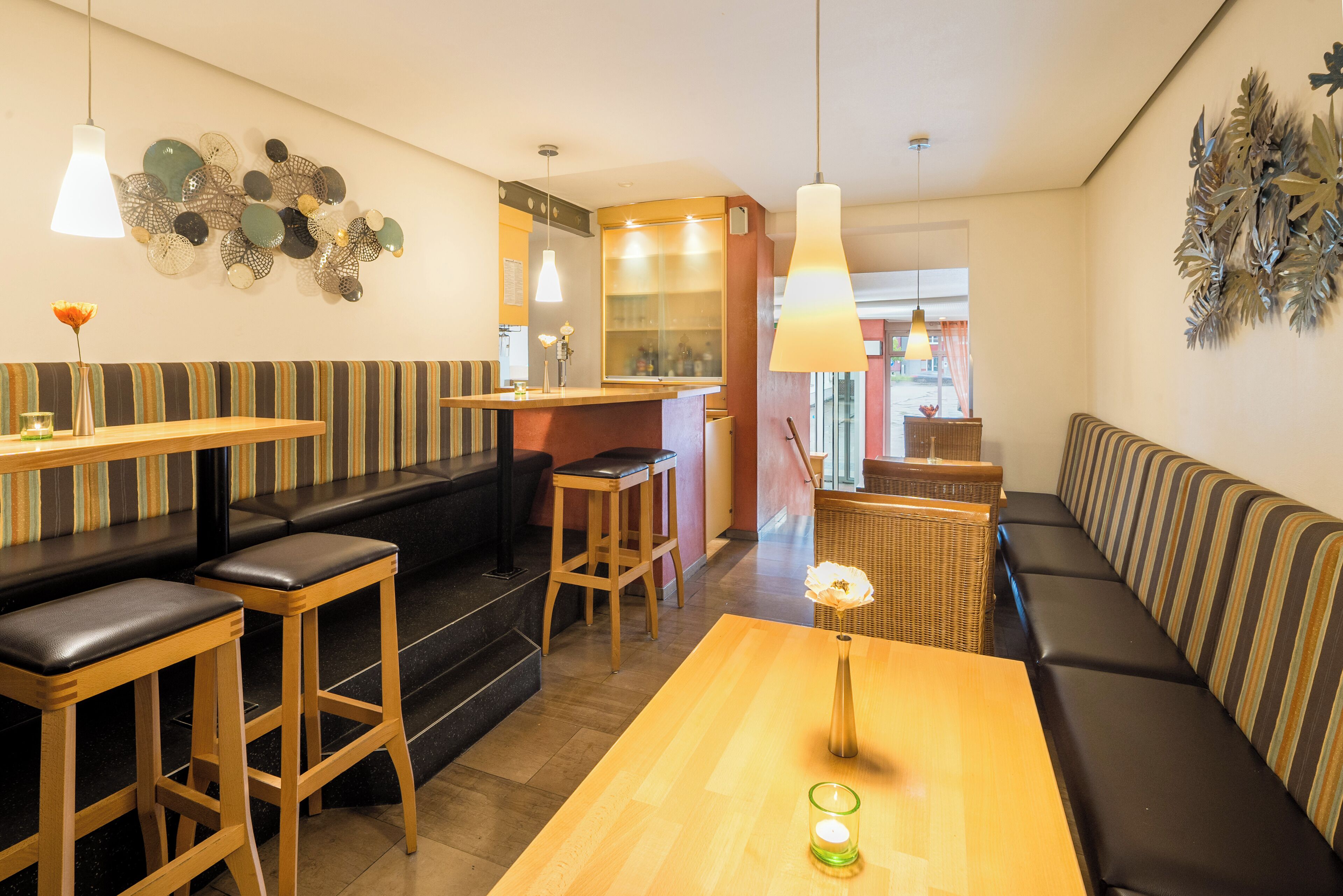 A cozy restaurant interior with striped booths, wooden tables, and hanging pendant lights.