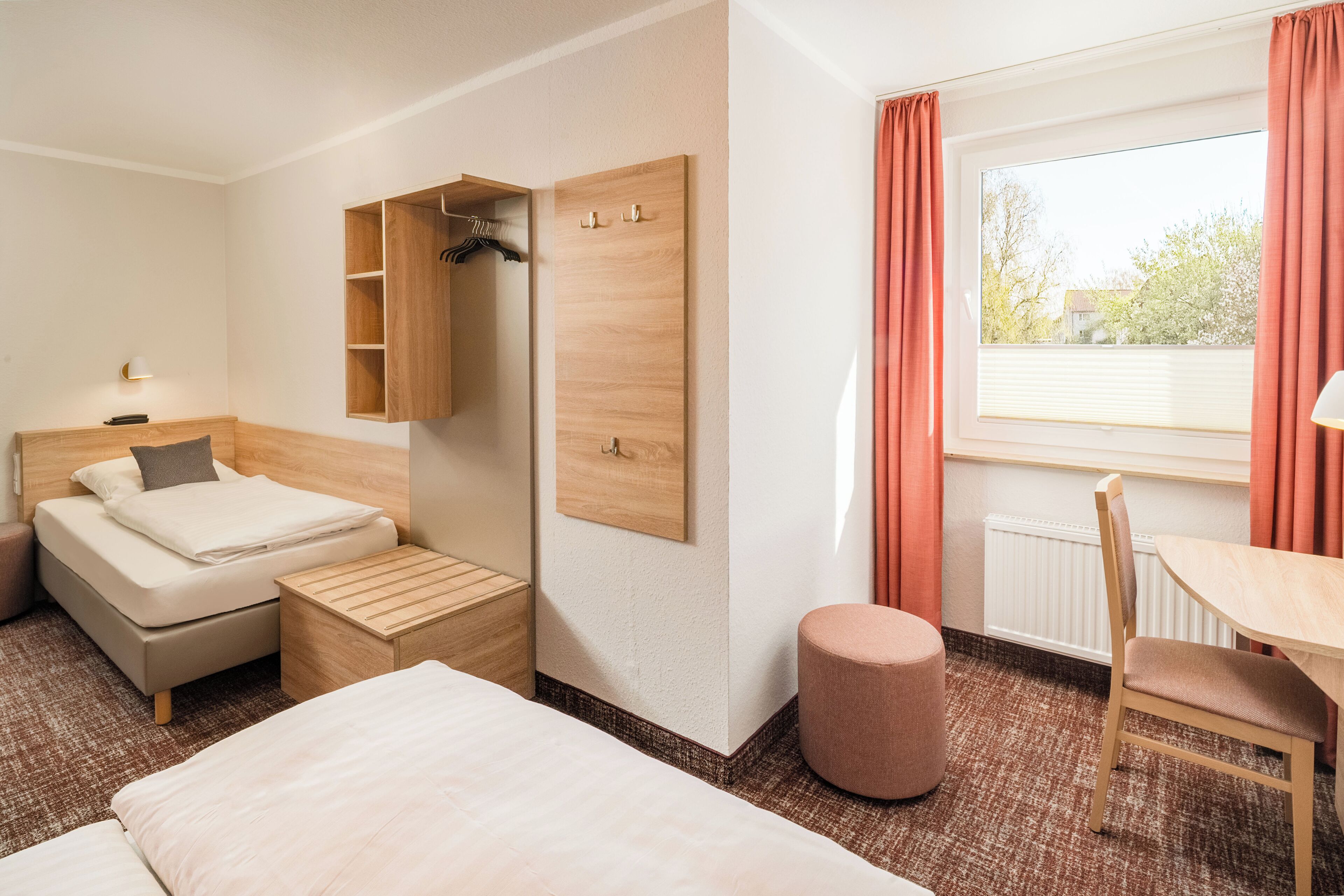 A hotel room with a bed, a desk, a chair, a wardrobe, and a window with curtains.
