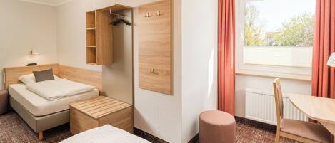 A hotel room with a bed, a desk, a chair, a wardrobe, and a window with curtains.