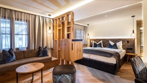Una habitación de hotel moderna con sofá, una mesa redonda de madera, una cama grande con cabecera y un armario de madera.