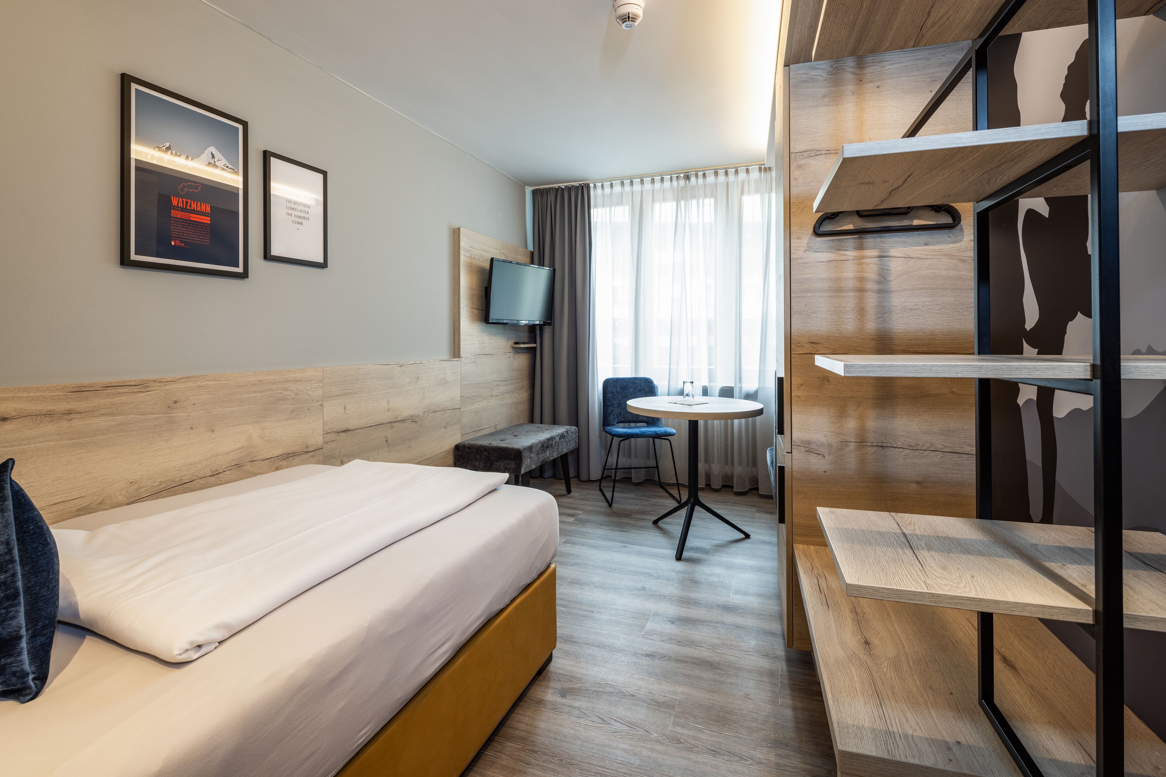 A hotel room with a bed, a desk, a chair, a television, and a window with curtains.