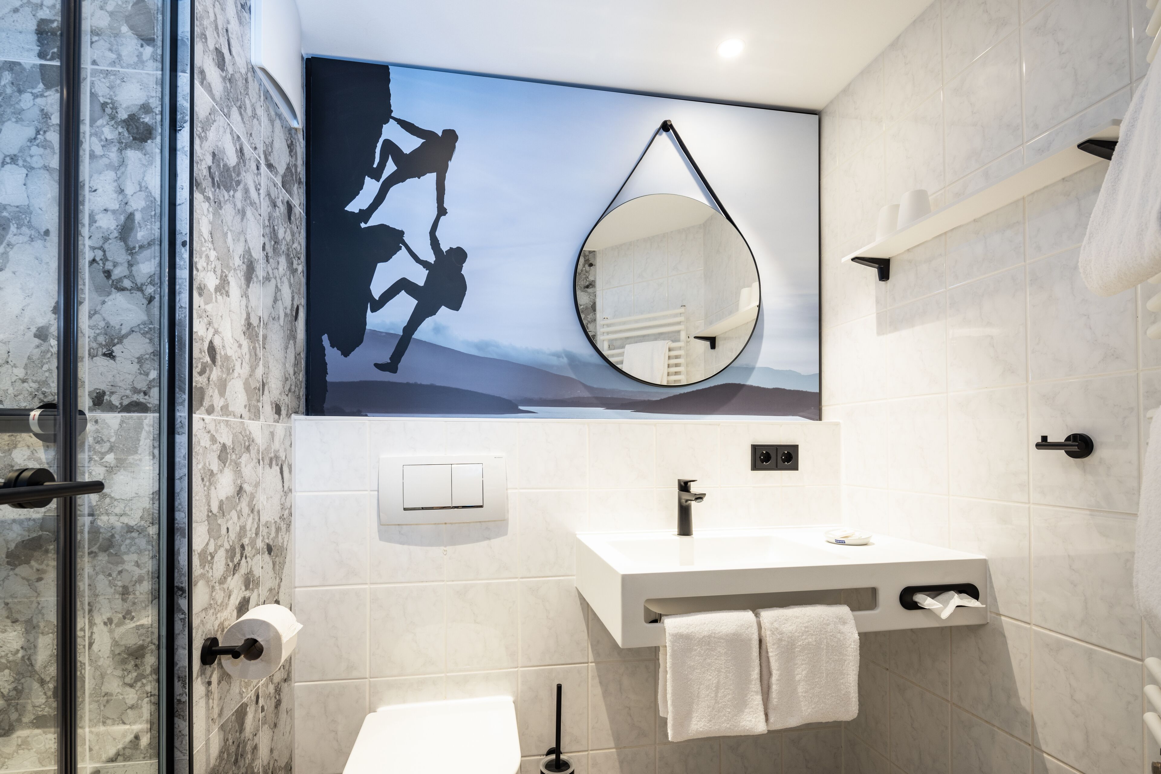 A modern bathroom with a glass shower enclosure, a white sink with a towel rack, and a large mirror.
